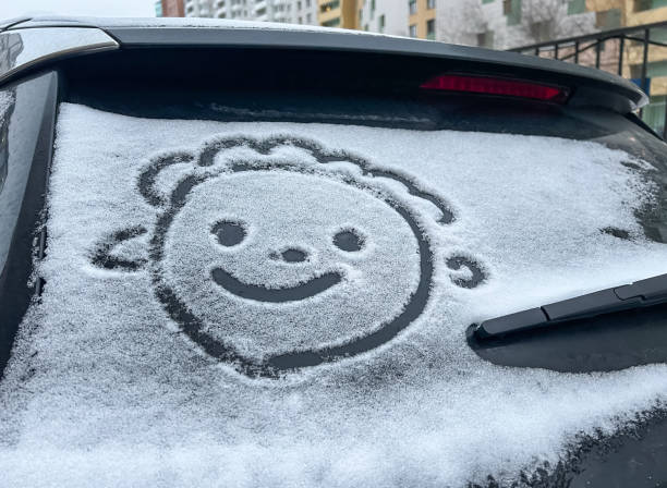 Drawing emoticon on a snowy car window. Funny face drawn on snow-covered car window. Smiling face (symbol) painted on snow above windshield wiper of car. Winter, transport concept.