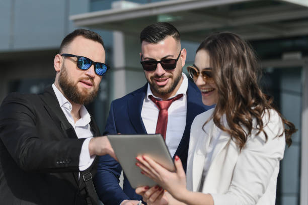 istock Joyful Colleagues Smiling While Reading Office Gossip on Tablet Standing in Front of Company 2201907905