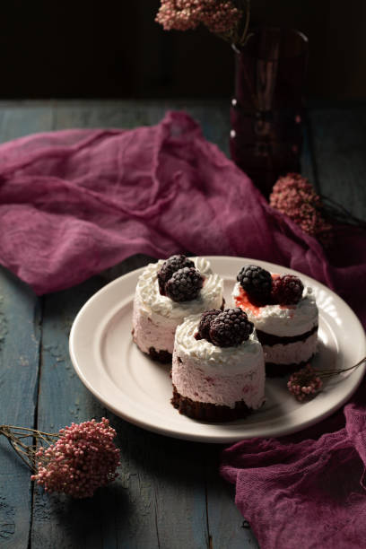 Delicious cream cakes with frozen blackberries on a white plate in a rustic style