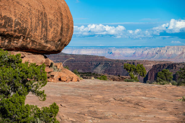 A stunning view of a balanced rock formation perched on the edge of the north rim of the Grand Canyon in Utah, overlooking vast layers of rock and deep valleys. The breathtaking desert landscape highlights the beauty of erosion and natural geology in the American Southwest.