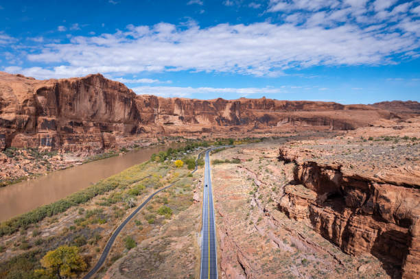 Aerial view overlooking the stunning landscapes of Moab, Utah, as a scenic highway winds along the Colorado River, framed by towering red rock cliffs. This iconic desert road trip offers breathtaking views, rugged terrain, and an unforgettable Southwest adventure.