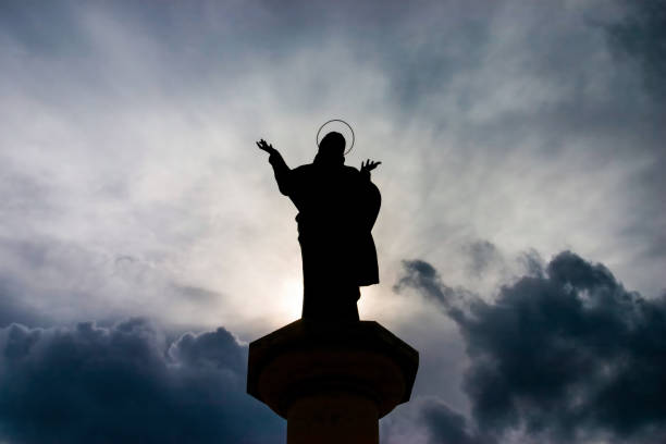 Silhouette of a statue of Jesus Christ with open arms, standing on a column against a backdrop of a cloudy sky