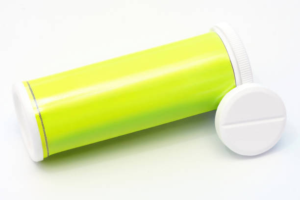 Close-up of a fluorescent yellow tube of effervescent medicine with its cap and a large white tablet lying on a white surface