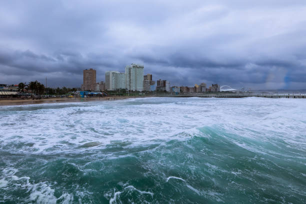Strong waves hit the shore while Durbans skyline looms in the background under overcast skies.