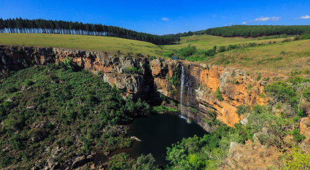 A breathtaking waterfall flows into a tranquil pool, fringed by verdant vegetation and rocky cliffs in South Africa.