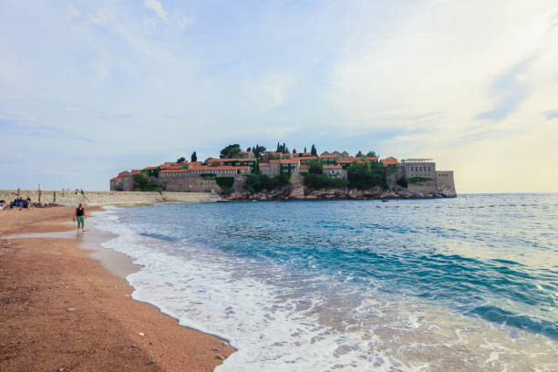 The sun sets over Sveti Stefan Island, highlighting its charming architecture and peaceful surroundings by the shoreline.