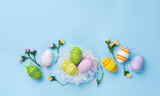 istock Easter decorated colored eggs. Painted eggs in a white nest and small flowers on a pastel blue background. Funny children background. Top view. Flat lay. 2201929106