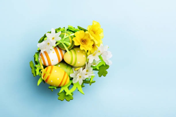 Easter basket with decorated colored eggs. Green felt basket with painted eggs and flowers on a pastel blue background. Top view
