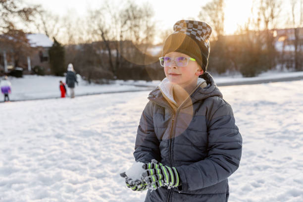 Cute little boy holds snowball while playing outdoors on winter day