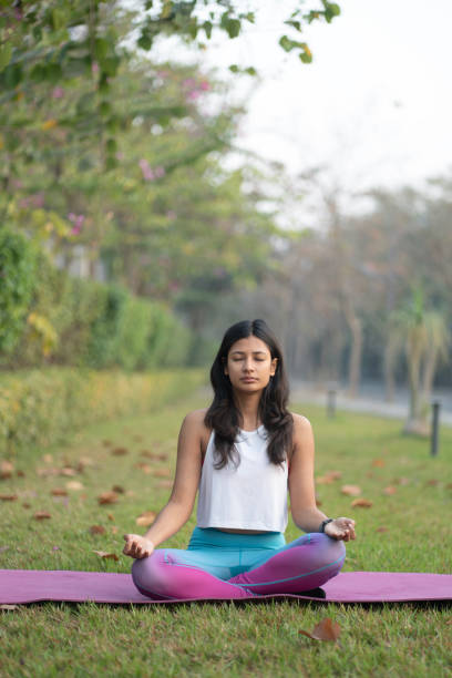 istock Woman practicing yoga in lotus position at park 2201940372