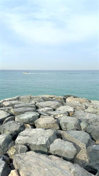 istock Massive stones form breakwater reaching toward vast ocean, waves gently lapping against rugged rocks, evoking serene coastal charm, relaxation, and timeless connection with nature concept. 2201942458