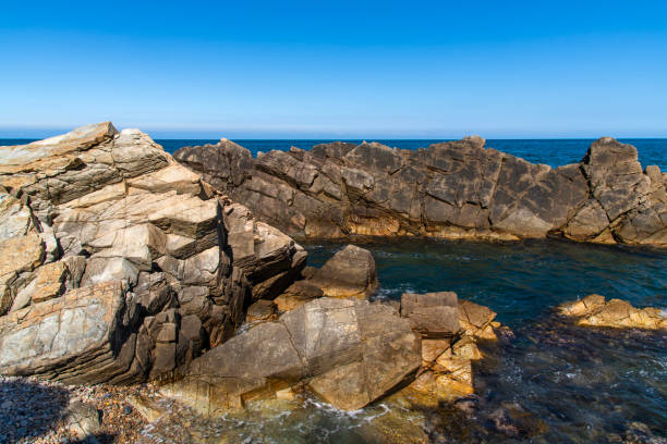Rocky coastline in a fjord in Western Norway at Golten (or Golta) in Sund municipality (near the city of Bergen) in Hordaland county on a sunny day in early springtime (April). The ground consists of foliated rock of gneiss (a coarse-grained metamorphic rock that forms under intense heat and pressure) and granite (coarse-grained (phaneritic) intrusive igneous rock) formation with cracks, slits, crevices and clefts. Shallow depth of field.