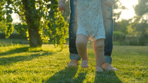istock Walking children's bare feet on a green lawn close-up. Child learns to take the first steps on the grass. Baby learns to walk with the help of his mother on a green grass in the park. 2201944220