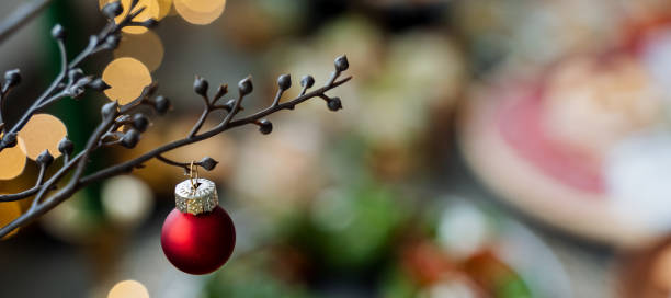 A bright red Christmas ball is currently hanging gracefully from a sturdy tree branch, adding a festive touch to the holiday ambiance around it, creating a joyful atmosphere