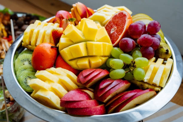 A beautifully arranged table showcases a stunning bowl that is filled to the brim with exquisitely sliced fresh fruit, creating a truly delightful sight and tempting treat for passersby