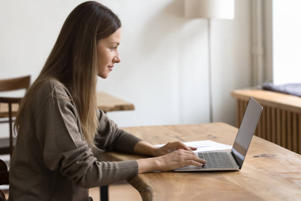 istock Side view focused woman sitting at table, working on laptop 2201951707