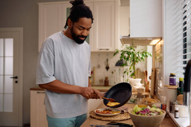 istock Smiling black man making omelet for breakfast in the kitchen. 2201953022