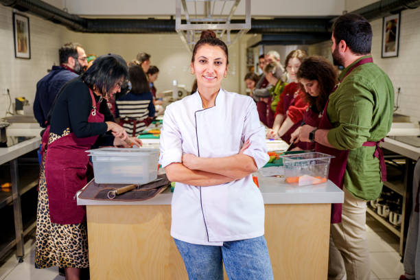 istock Professional Chef who teaches hands-on cooking in a modern kitchen poses for the camera as his students work 2201954753
