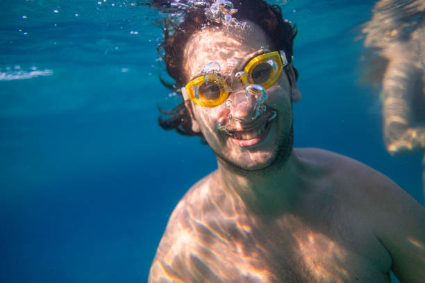 Young man diving in the sea with yellow goggles and releasing air bubbles