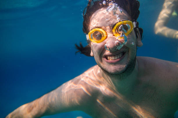A young man, underwater, grins and looks at the camera