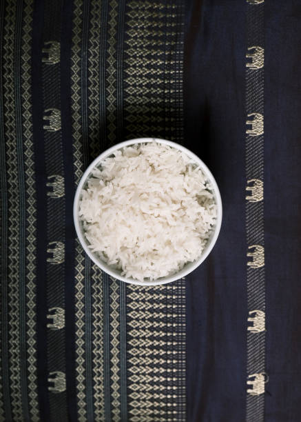 A simple yet elegant bowl of steamed jasmine rice placed on a traditional Thai woven fabric adorned with intricate elephant patterns. The top-down perspective emphasizes the texture of the fluffy rice and the cultural significance of the fabric, making it a visually rich representation of Thai cuisine. Ideal for use in food blogs, travel content, cultural documentaries, and restaurant branding.