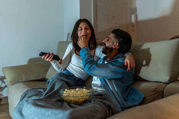 istock Young couple watching television and sharing popcorn on sofa at night 2201967616