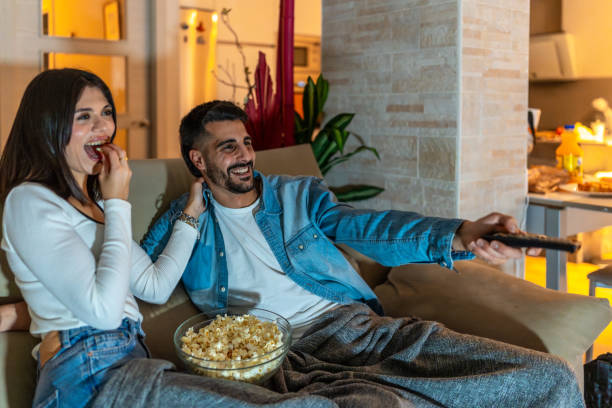 istock Young couple watching tv and eating popcorn on sofa at night 2201967627