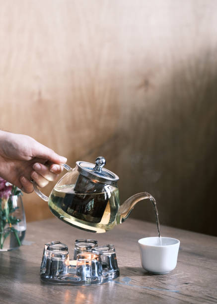 istock Pouring hot herbal tea from a glass teapot into a white ceramic cup, Cozy tea time moment on a wooden table with natural light, Relaxation and mindfulness concept 2201967824