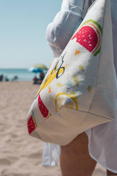 istock Woman holding summer themed tote bag walking on the beach 2201972785
