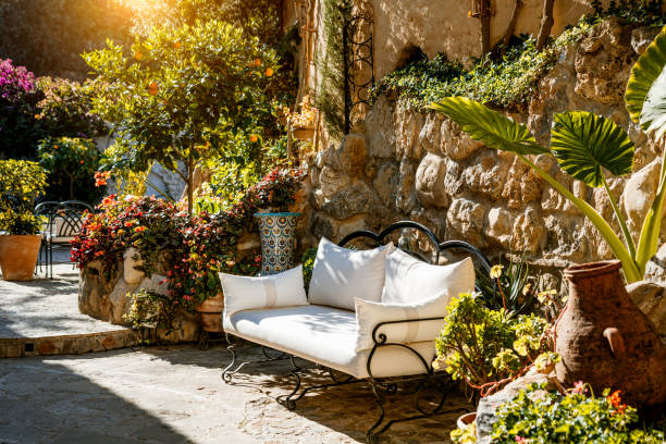 Idyllic courtyard with vibrant plants, rustic stone walls, and cozy seating, showcasing a tranquil Mediterranean ambiance bathed in sunlight.
