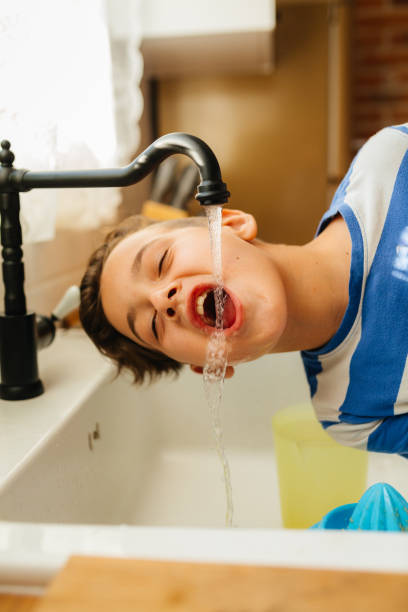 istock Boy Playfully Drinking Water from a Kitchen Faucet 2201982667