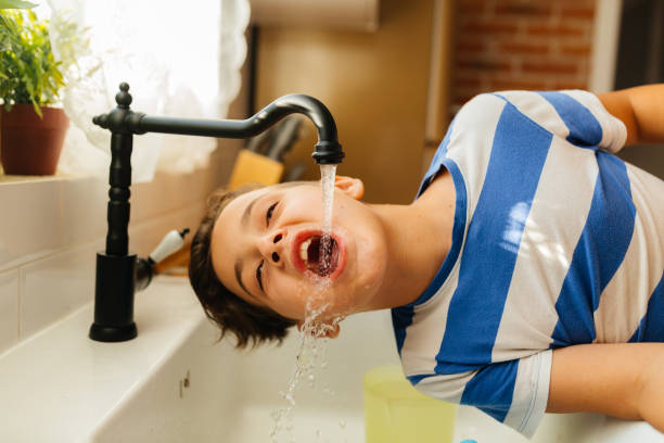 istock Boy Playfully Drinking Water from a Kitchen Faucet 2201982715