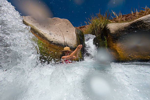 Woman by natural rock formation in waterfall pool. Adventurous outdoor activity in scenic landscape. Thrill-seeker exploring nature’s wonders.