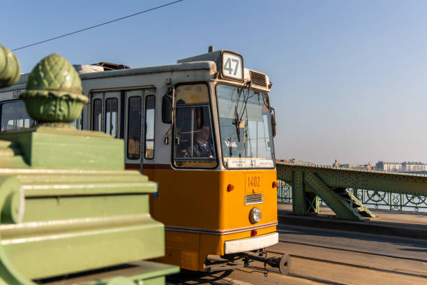 02/17/2025, Budapest. Yellow tram number 47 crossing the Margaret Bridge in Budapest, Hungary, with a tram driver driving the vehicle and the Danube river in the background