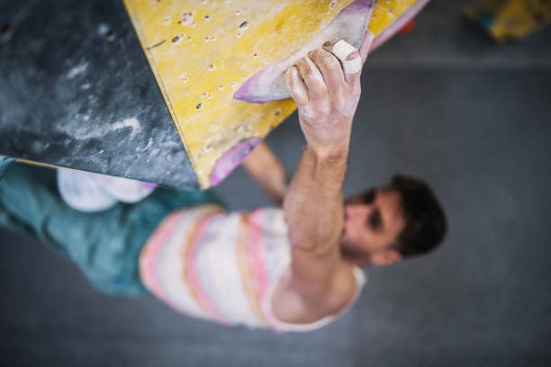 Athletic male climber training his skills and endurance on a indoor bouldering wall with colorful grips.