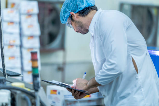 istock A food processing supervisor wearing protective gear and holding a clipboard, inspecting machinery on a production line, emphasizing quality control, safety, and efficiency in industrial operations. 2201990857