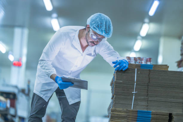 istock A food processing supervisor in protective gear inspecting packaging materials in a factory, holding a clipboard, emphasizing quality control, hygiene, and safety in food production operations 2201990991