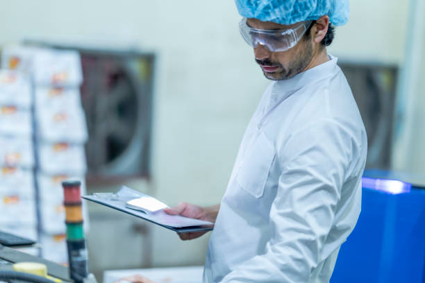 istock A food processing supervisor wearing protective gear and holding a clipboard, inspecting machinery on a production line, emphasizing quality control, safety, and efficiency in industrial operations. 2201991040