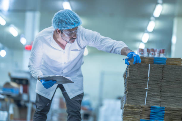 istock A food processing supervisor in protective gear inspecting packaging materials in a factory, holding a clipboard, emphasizing quality control, hygiene, and safety in food production operations 2201991251