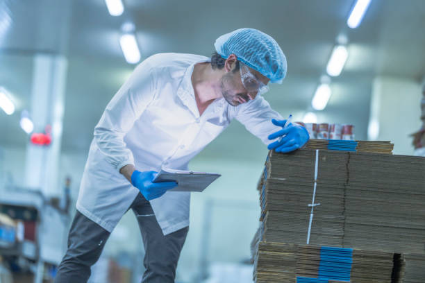 istock A food processing supervisor in protective gear inspecting packaging materials in a factory, holding a clipboard, emphasizing quality control, hygiene, and safety in food production operations 2201991482