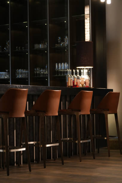 istock A row of bar stools lined up against a sleek bar counter with illuminated shelves displaying glassware and bottles 2201998692