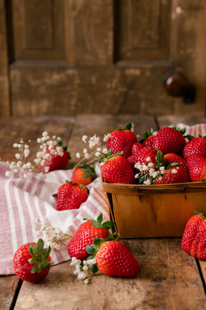 istock Fresh strawberries in a wooden basket with flowers on a rustic table. 2202009388