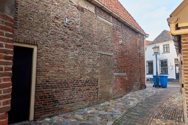Hasselt, Netherlands: A narrow historic alley with cobblestone pavement, a brick archway, and an old Dutch house near the water.