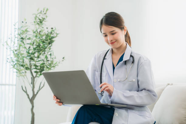 istock A doctor in a white lab coat is sitting on a couch, working on a laptop. 2202030889