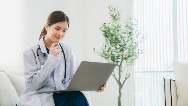 istock A doctor in a white lab coat is sitting on a couch, working on a laptop. 2202031043