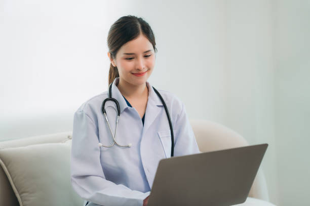 istock A doctor in a white lab coat is sitting on a couch, working on a laptop. 2202031099