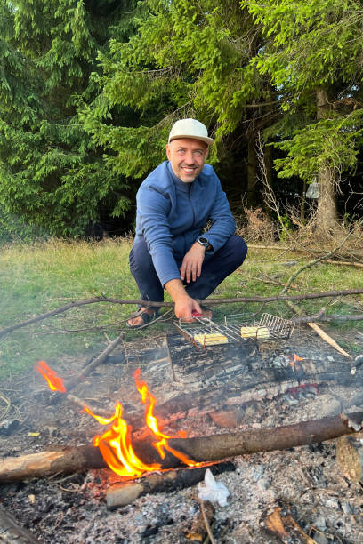 istock Man tourist smiling while grilling food over campfire in forest clearing 2202031326