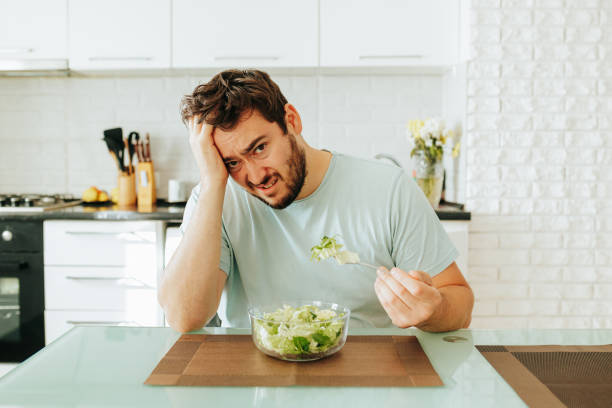 istock Man looking frustrated while eating salad in a modern kitchen 2202033448
