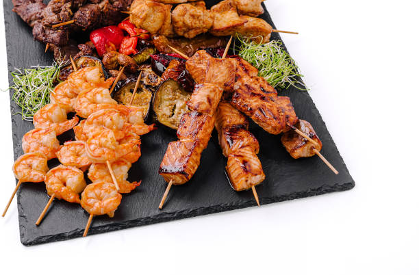 istock Grilled skewers featuring shrimp, beef, and chicken served on a slate platter with vegetables 2202034271