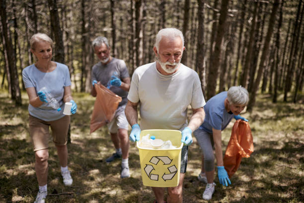Group of mature friends cooperating while cleaning and recycling garbage from the forest. Copy space.